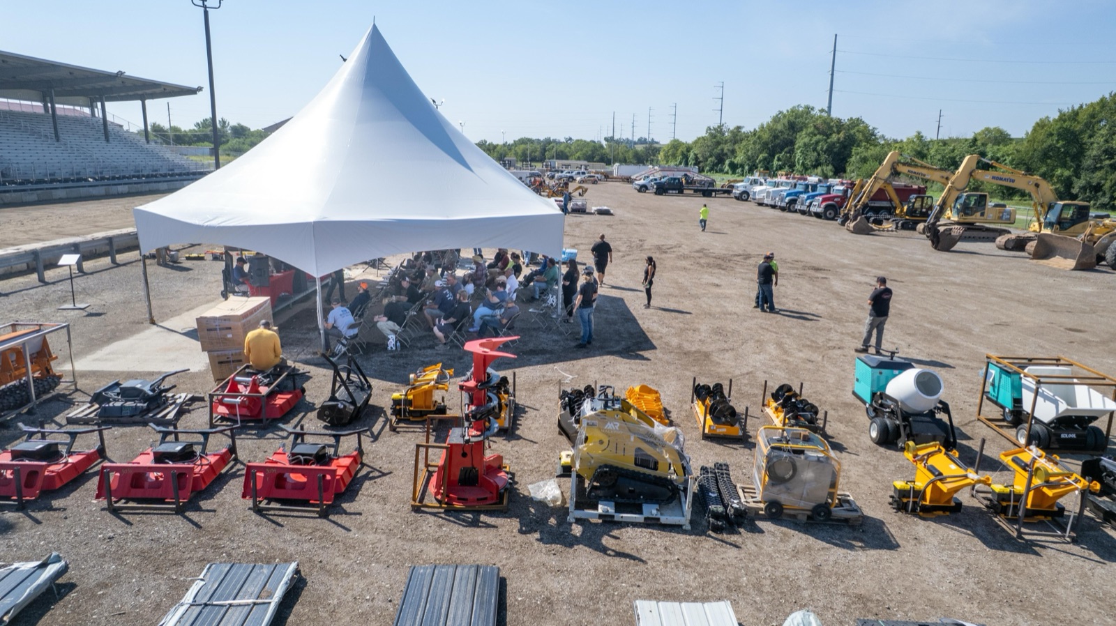Bidders seated under the auction tent with equipment lined up behind